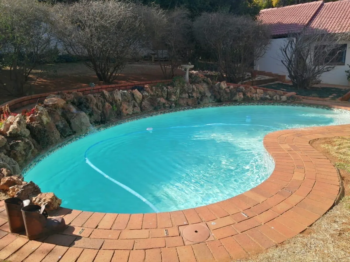 Finished curved pool with red brick paving and stone wall