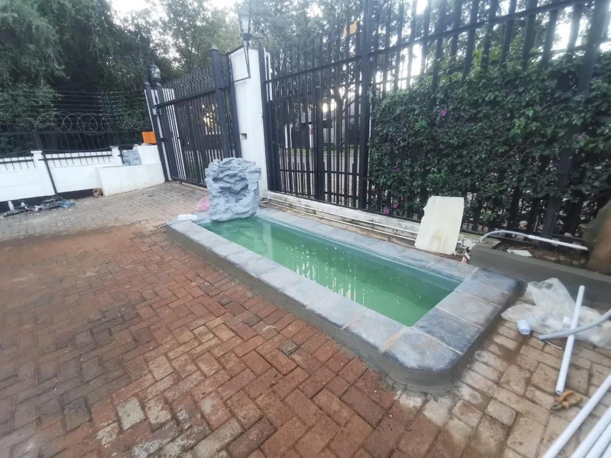 Small pool built beside a driveway gate with a rock feature